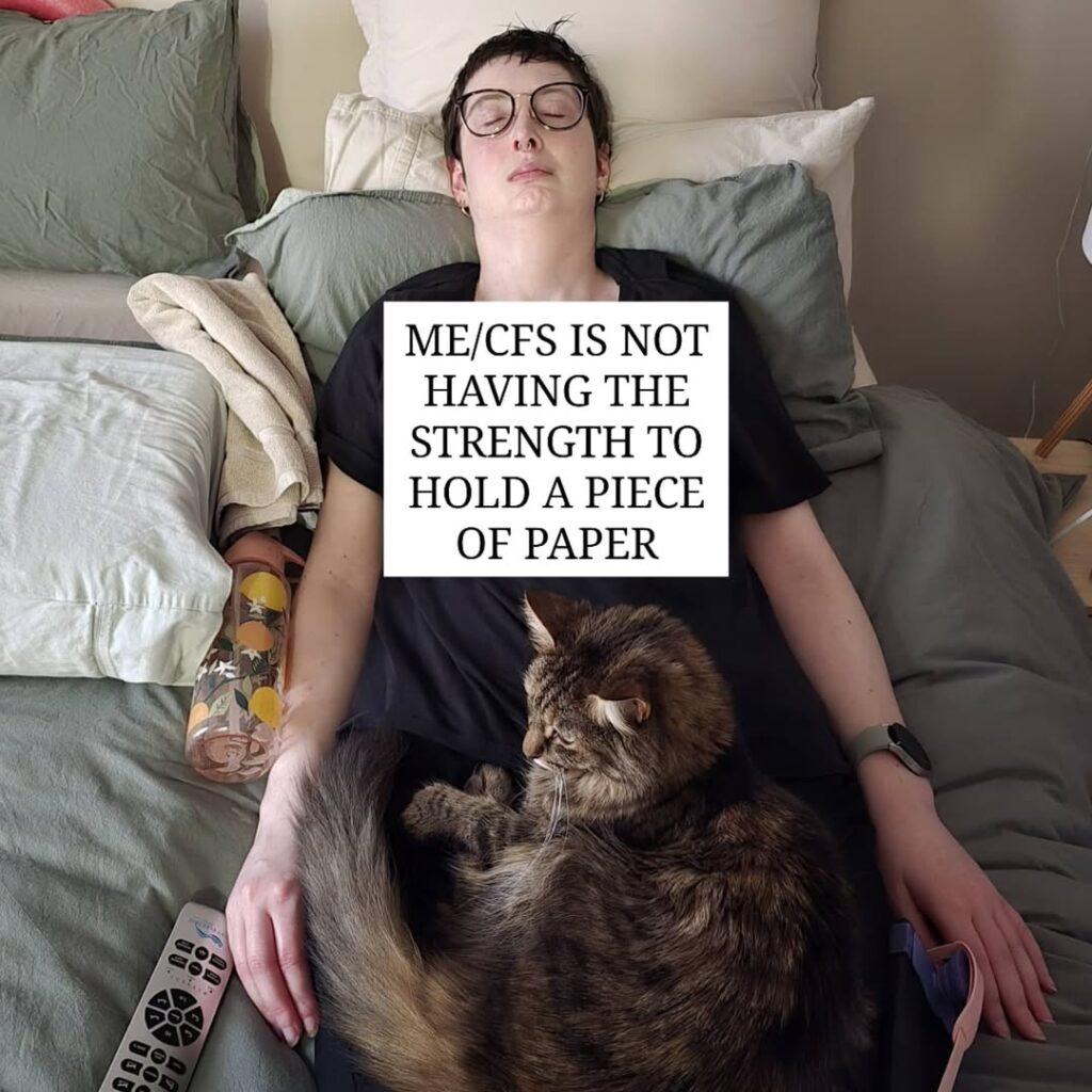 Siobhan is holding a sign that reads: “ME/CFS is not having the strength to hold a piece of paper.