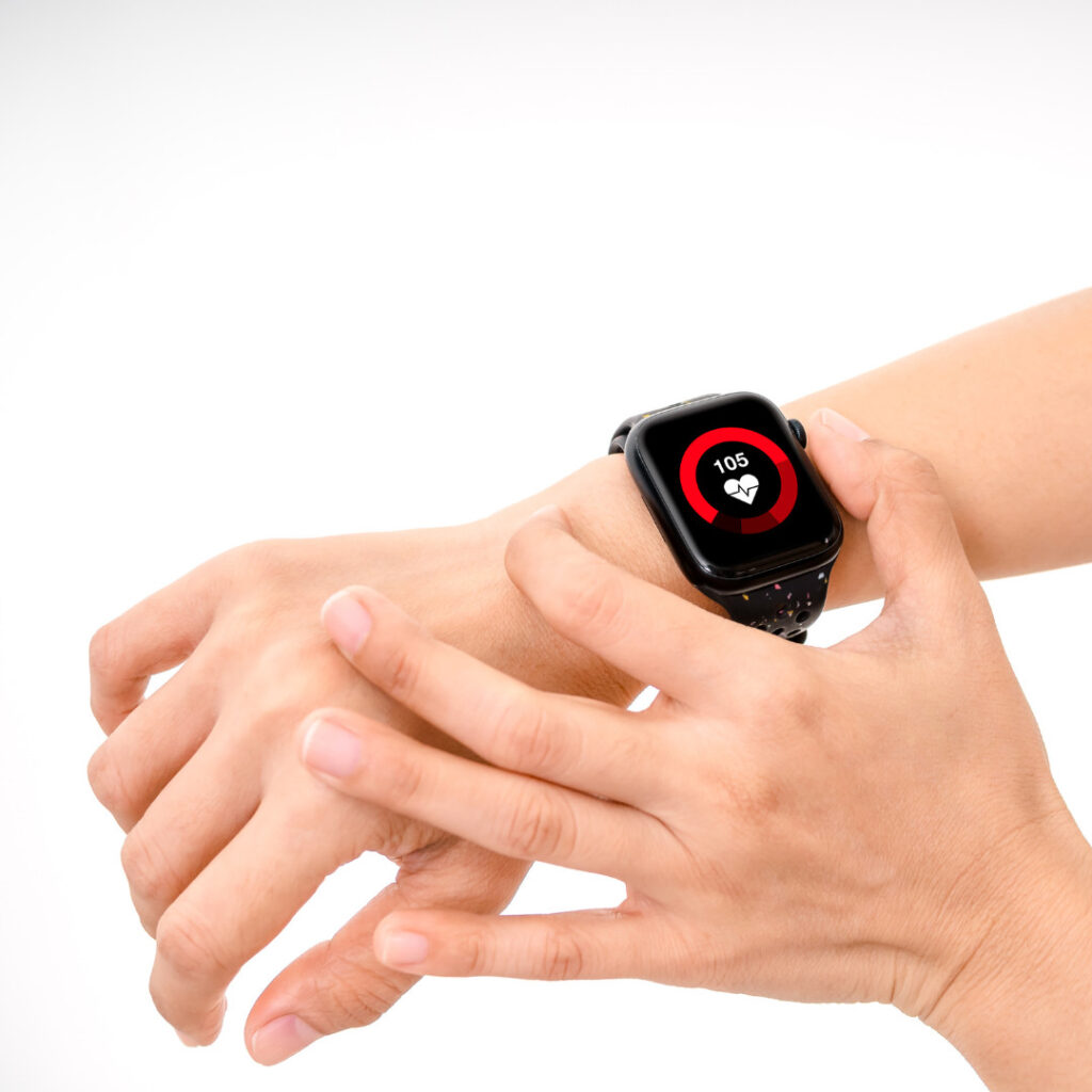 A close-up of a person’s wrist wearing a black smartwatch. The watch display shows a heart rate reading of 105 beats per minute, highlighted by a red circular graphic around a heart icon
